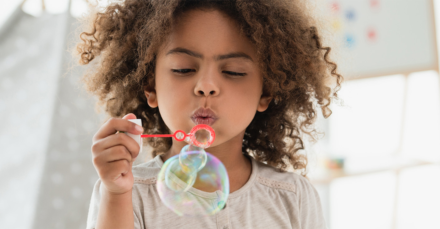 A curly A-frican-American kid blowing soap bubbles.