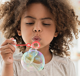 An African-American kid blowing a soap bubble.